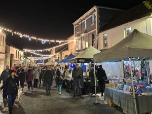 An image of Ivybridge Christmas Festival, showing lots of people in the street with the Christmas lights and various trade stalls.