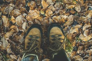 Looking down at hiking boots in a pile of leaves, representing walking on the Slow Ways