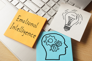 Image shows 3 post-it notes on a laptop. One note says 'emotional intelligence', one has a picture of a lightbulb, and one has a picture of a head with cogs whirring inside.